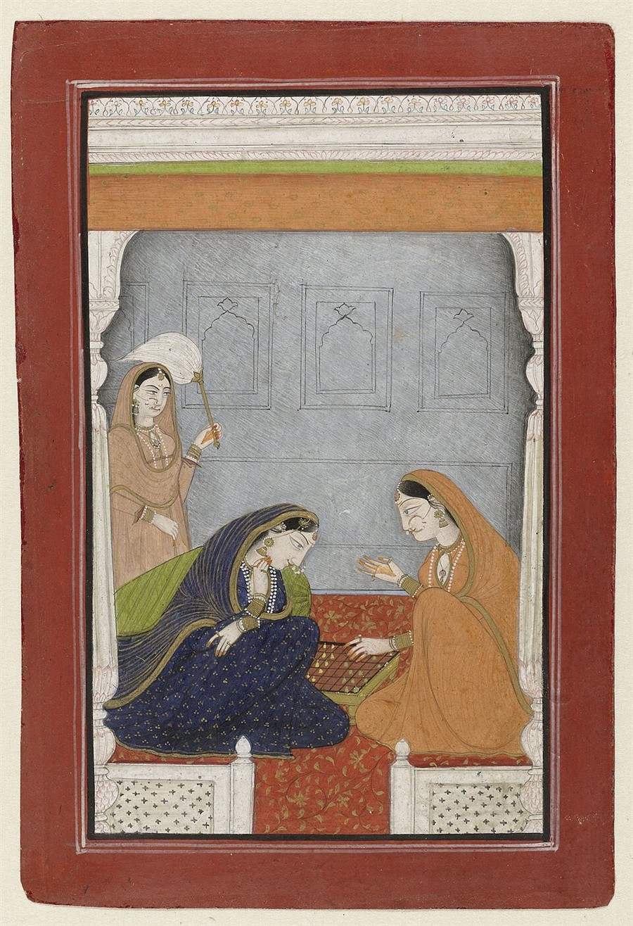 Indian miniature painting: two women sit on a red carpet playing chaturanga on a small board, one in indigo and one in orange, while an attendant holds a fan.